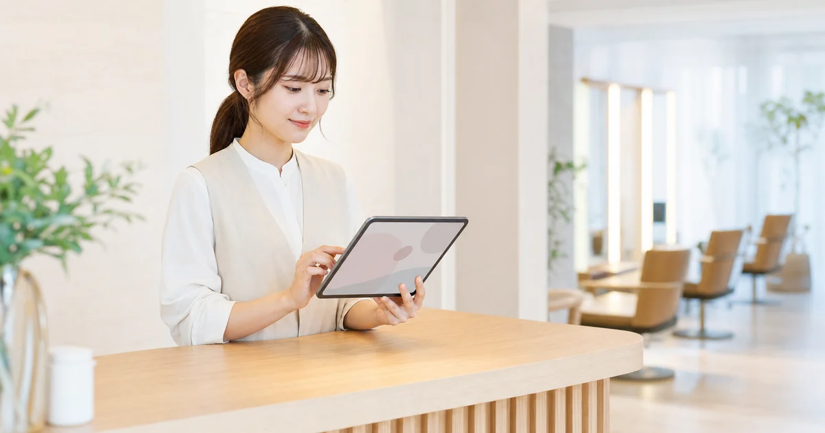 サロンの受付でタブレットを操作しながら顧客対応をするスタッフ